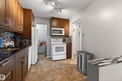 Kitchen featuring wood-finish cabinetry, dark countertops, and a mosaic tile backsplash - 35 3111 142 Avenue, Edmonton, AB 