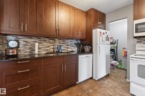Kitchen featuring rich wood-finish cabinetry, dark countertops, and a mosaic tile backsplash - 35 3111 142 Avenue, Edmonton, AB 