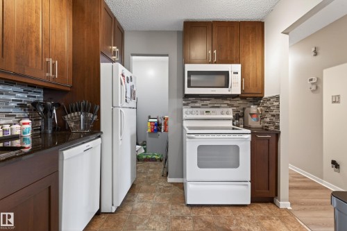 Kitchen featuring wood-finish cabinetry, dark countertops, and a mosaic tile backsplash - 35 3111 142 Avenue, Edmonton, AB 