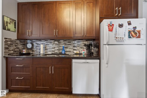 Kitchen featuring rich wood-finish cabinetry, dark countertops, and a mosaic tile backsplash - 35 3111 142 Avenue, Edmonton, AB 