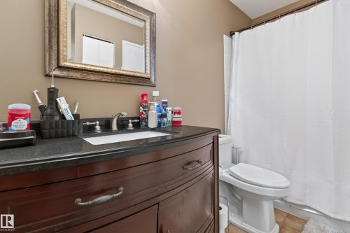 Bathroom featuring a dark wood-finish vanity with a dark countertop, an integrated sink with a brushed nickel faucet, and a decorative framed mirror - 35 3111 142 Avenue, Edmonton, AB 