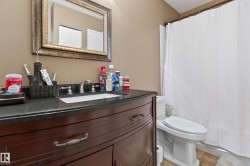 Bathroom featuring a dark wood-finish vanity with a dark countertop, an integrated sink with a brushed nickel faucet, and a decorative framed mirror - 
