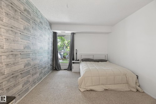 Textured accent wall featuring a wood-look finish, light-colored carpeting, and a window with outdoor greenery - 35 3111 142 Avenue, Edmonton, AB 