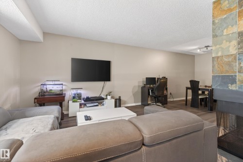 Living area featuring wood-finish flooring, a stone-clad fireplace with a dark hearth, and neutral wall tones - 35 3111 142 Avenue, Edmonton, AB 