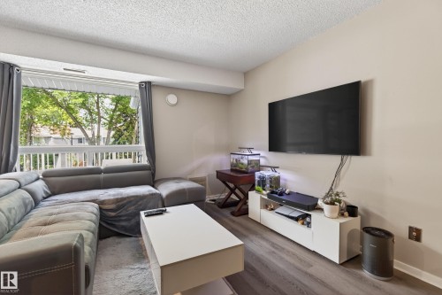 Living area featuring wide plank wood-finish flooring, a neutral wall color, and a large window with a white railing balcony - 35 3111 142 Avenue, Edmonton, AB 