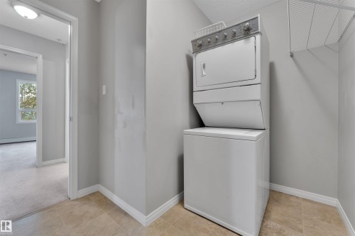 Dedicated laundry area featuring a white stacked washer and dryer, tile flooring, and wire shelving - 3302 9351 Simpson Drive, Edmonton, AB 