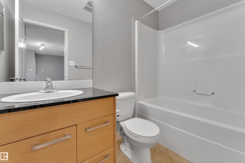 Bathroom featuring a wood-finish vanity with a built-in sink, a dark countertop, a mirror, and a combined shower and tub unit - 3302 9351 Simpson Drive, Edmonton, AB 