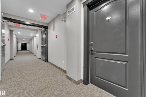 Building corridor featuring light-colored patterned carpet flooring, gray walls, and dark trim - 3302 9351 Simpson Drive, Edmonton, AB 