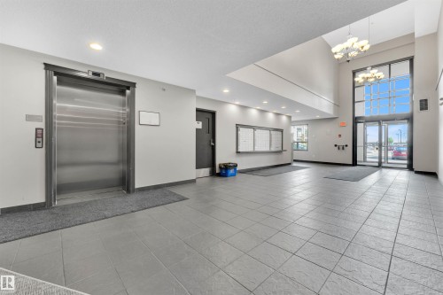 Spacious lobby with a vaulted ceiling, large transom windows, contemporary chandelier, stainless steel elevator, and grey tile flooring - 3302 9351 Simpson Drive, Edmonton, AB 