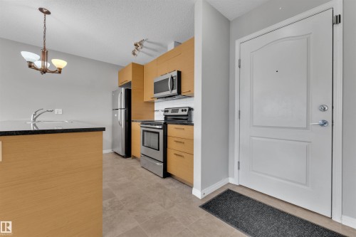 Kitchenette featuring wood-finish cabinetry, stainless steel appliances, and a dark stone-finish countertop - 3302 9351 Simpson Drive, Edmonton, AB 