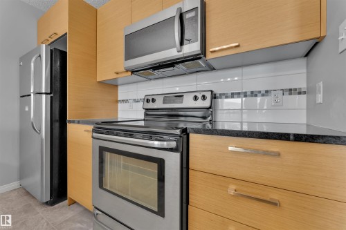 Kitchen featuring stainless steel appliances, light wood-finish cabinetry, dark countertops, white subway tile backsplash, and a decorative mosaic tile accent strip - 3302 9351 Simpson Drive, Edmonton, AB 