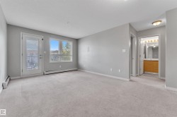 Spacious living area featuring light gray carpeting, neutral wall tones, and a glass-paneled door leading to a balcony - 