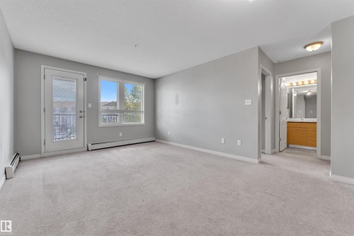 Spacious living area featuring light gray carpeting, neutral wall tones, and a glass-paneled door leading to a balcony - 3302 9351 Simpson Drive, Edmonton, AB 
