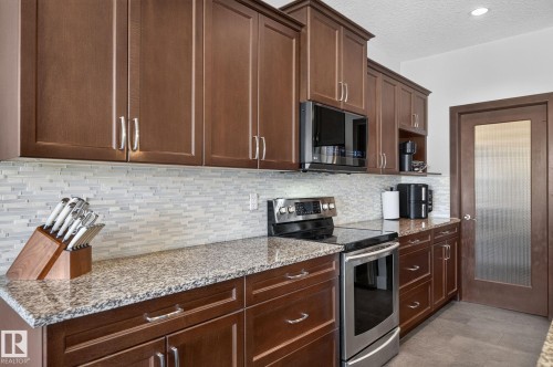 Kitchen featuring wood cabinetry, granite-style countertops, and a mosaic tile backsplash - 14016 161 Avenue, Edmonton, AB 
