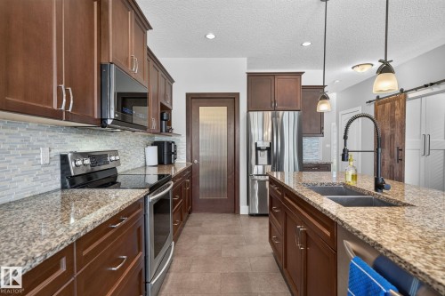 Gourmet kitchen featuring granite countertops, stainless steel appliances, dark wood cabinetry, a tile backsplash, and a large central island with sink - 14016 161 Avenue, Edmonton, AB 