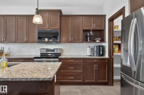 Kitchen featuring wood-finish cabinetry, granite countertops, and a full tile backsplash - 14016 161 Avenue, Edmonton, AB 