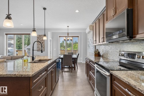Open-concept kitchen featuring granite countertops, wood cabinetry, a tile backsplash, and stainless steel appliances - 14016 161 Avenue, Edmonton, AB 