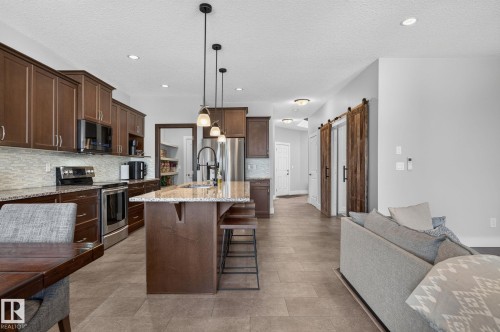 Contemporary kitchen featuring dark wood cabinetry, stainless steel appliances, and a central island with a light-toned countertop - 14016 161 Avenue, Edmonton, AB 