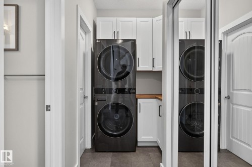 Dedicated laundry area featuring a stacked washer and dryer, white cabinetry with black hardware, and wood-finish countertops - 14016 161 Avenue, Edmonton, AB 
