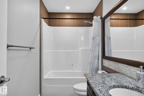 White tub and shower combination with a granite-patterned countertop, wood-finish vanity, and mosaic tile backsplash - 14016 161 Avenue, Edmonton, AB 