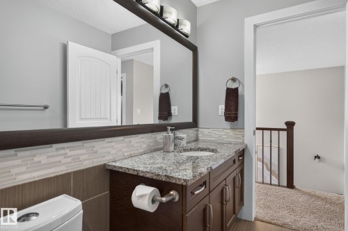 Bathroom vanity featuring a granite countertop with integrated sink, dark wood-finish cabinetry, and a mosaic tile backsplash - 14016 161 Avenue, Edmonton, AB 