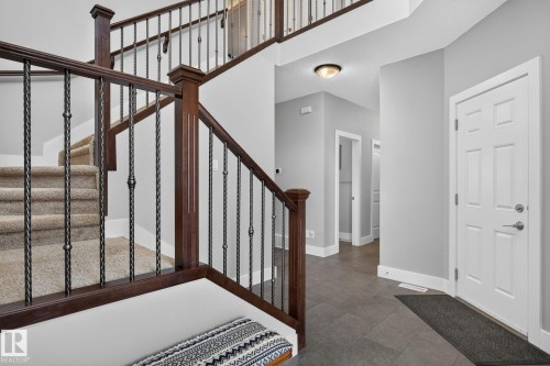 Entryway featuring a grand staircase with dark wood-finish newel posts and wrought iron balusters, complemented by light grey wall paint and white baseboards - 14016 161 Avenue, Edmonton, AB 