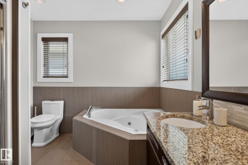 Bathroom featuring a corner soaking tub, a single vanity with stone countertop and integrated sink, a tiled wainscoting, and wood-finish flooring - 14016 161 Avenue, Edmonton, AB 