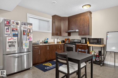 Full kitchen with wood-finish cabinetry, stainless steel appliances, and a compact dining area - 14016 161 Avenue, Edmonton, AB 