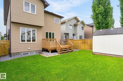 Spacious backyard featuring a manicured lawn, a two-story residence with tan siding, a wooden deck with stairs, a privacy fence, and a storage shed - 14016 161 Avenue, Edmonton, AB 