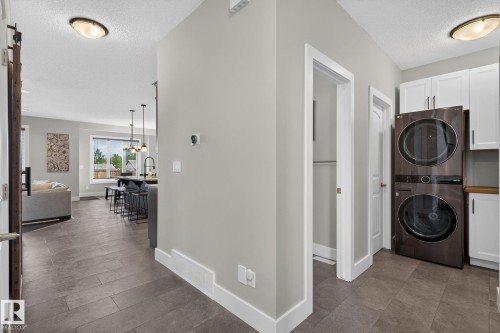 Dedicated laundry area featuring a stacked washer and dryer, white shaker cabinetry, and a wood-finish countertop - 14016 161 Avenue, Edmonton, AB 