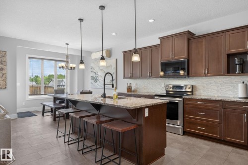 Open-concept kitchen featuring an oversized island with pendant lighting, stainless steel appliances, extensive cabinetry, and a textured tile backsplash - 14016 161 Avenue, Edmonton, AB 