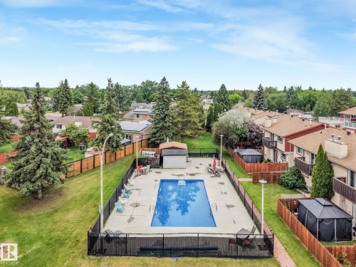 Private outdoor swimming pool with surrounding concrete deck, black metal fencing, and a small pool house - 2921 130 Avenue, Edmonton, AB 