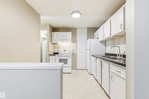 Galley kitchen featuring white cabinetry, dark countertops, and a full suite of white appliances including a refrigerator, dishwasher, and range - 2005 Saddleback Road, Edmonton, AB - Indoor Photo Showing Kitchen With Double Sink