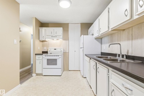 Kitchen featuring white cabinetry, dark countertops, a double basin stainless steel sink, white electric range, and a white refrigerator - 2005 Saddleback Road, Edmonton, AB - Indoor Photo Showing Kitchen With Double Sink