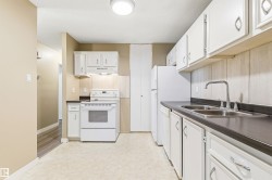 Kitchen featuring white cabinetry, dark countertops, a double basin stainless steel sink, white electric range, and a white refrigerator - 