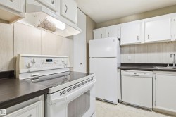 Kitchen featuring white cabinetry, dark countertops, a built-in range, a refrigerator, and a dishwasher - 