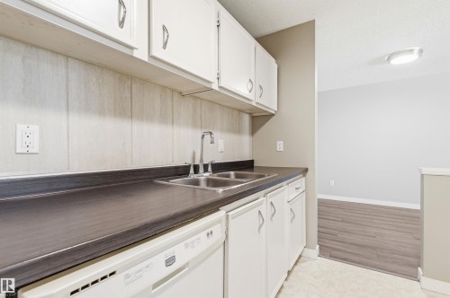 Kitchen area featuring white cabinetry, a double basin stainless steel sink, a dark countertop, an integrated dishwasher, and a light-toned backsplash - 2005 Saddleback Road, Edmonton, AB - Indoor Photo Showing Kitchen With Double Sink