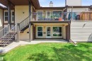 Multi-level exterior featuring light-colored siding, a second-story balcony with dark railings, a ground-level patio, and a staircase providing access to the upper unit - 2005 Saddleback Road, Edmonton, AB  - Outdoor With Deck Patio Veranda With Exterior 