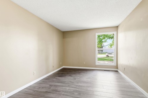 Spacious room featuring wood-finish flooring, neutral-toned walls, white baseboards, and a large window providing natural light - 2005 Saddleback Road, Edmonton, AB - Indoor Photo Showing Other Room