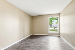 Spacious room featuring wood-finish flooring, neutral-toned walls, white baseboards, and a large window providing natural light - 