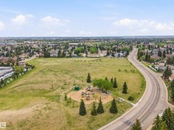 Expansive green space featuring a playground with multiple structures, mature evergreen and deciduous trees, and paved pedestrian paths - 