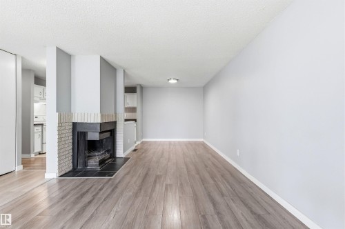 Living area featuring wood-finish flooring, a brick-surround fireplace with a black tile hearth, neutral wall tones, and a flush-mount ceiling light - 2005 Saddleback Road, Edmonton, AB - Indoor With Fireplace
