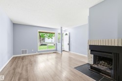 Spacious living area featuring wood-finish flooring, a fireplace with stone surround and hearth, light blue walls, and a large front-facing window - 