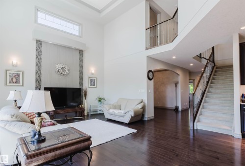 Spacious living area featuring high ceilings, wood-finish flooring, and a carpeted staircase with metal and wood railing - 4377 Mcclung Crescent, Edmonton, AB 