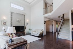 Spacious living area featuring high ceilings, wood-finish flooring, and a carpeted staircase with metal and wood railing - 