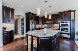 Gourmet kitchen featuring dark wood cabinetry, stainless steel appliances, a center island with a stone countertop, a tile backsplash, and wood-finish flooring - 