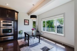 Dining area featuring dark wood-finish flooring, a contemporary black drum pendant light, and a large window overlooking mature greenery - 