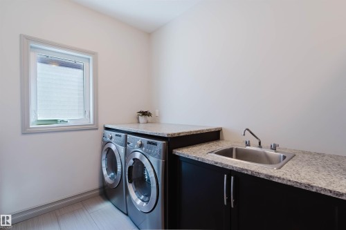 Laundry area featuring a window, granite-finish countertops, dark cabinetry, and a stainless steel utility sink - 4377 Mcclung Crescent, Edmonton, AB 