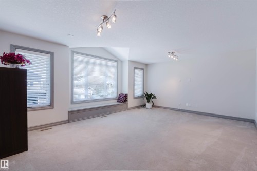 Spacious room featuring multiple windows with horizontal blinds, track lighting, and soft carpeting - 4377 Mcclung Crescent, Edmonton, AB 
