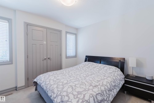 Bedroom featuring light gray walls, plush carpeting, two windows with blinds, a ceiling-mounted light fixture, and a built-in double-door closet with gray paneled doors - 4377 Mcclung Crescent, Edmonton, AB 